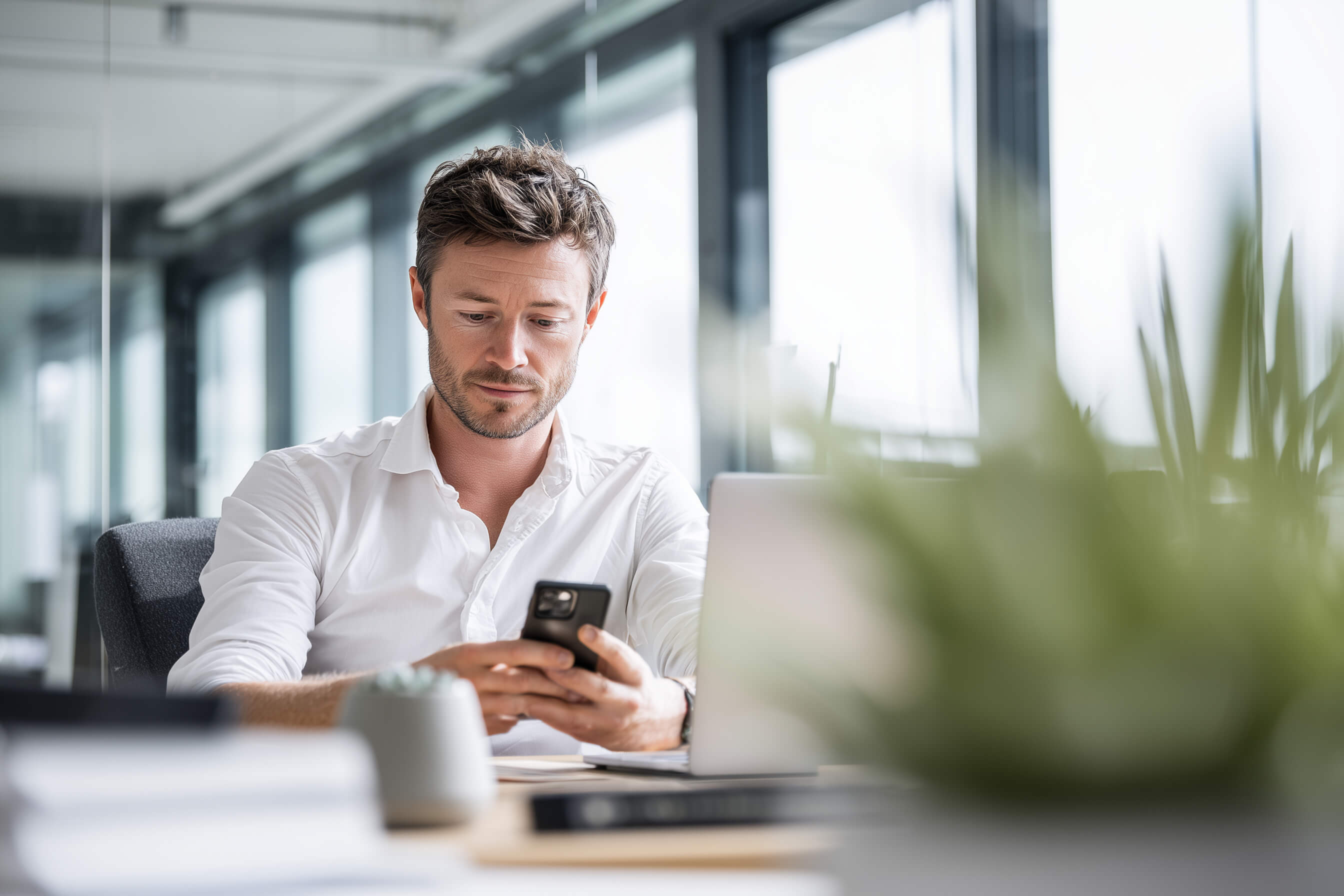 Man using a smartphone and laptop in an office setting - Desk and Device